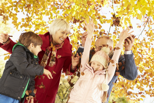 A happy laughing family throwing around brown and yellow leaves while under an autumn tree