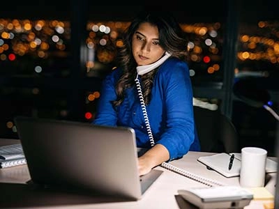 A woman working late at night in an office, talking on the phone.